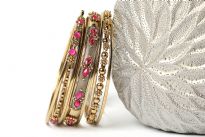 Antique gold colored 8 pieces fashion bangles set has fuchsia beads on 2 of the bangles which gives an edge to this set. 5 thin bangles with 2 bangles have metal floral pattern & one wide bangle has fuchsia stones. Hand crafted in India by expert artisans.  
